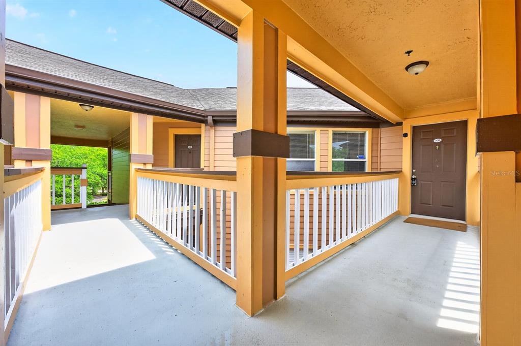 An outdoor covered walkway features a brown door, white railings, and yellow support columns — 474 S PIN OAK PLACE UNIT 308, LONGWOOD, FL