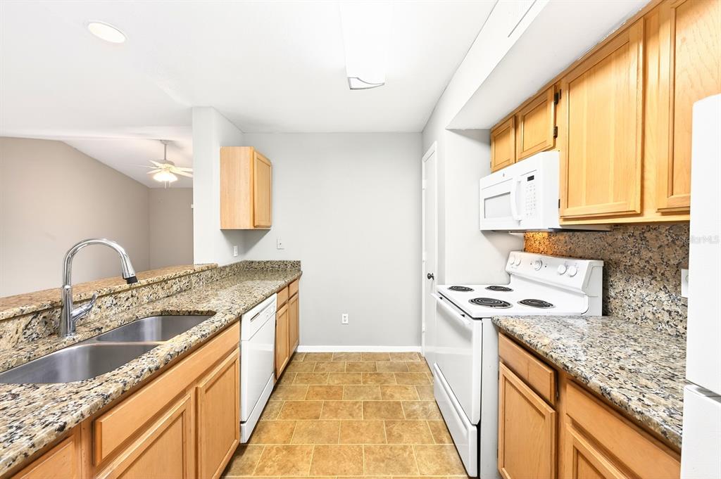 A kitchen features light wood cabinets, granite countertops, white appliances, and tan tile flooring — 474 S PIN OAK PLACE UNIT 308, LONGWOOD, FL