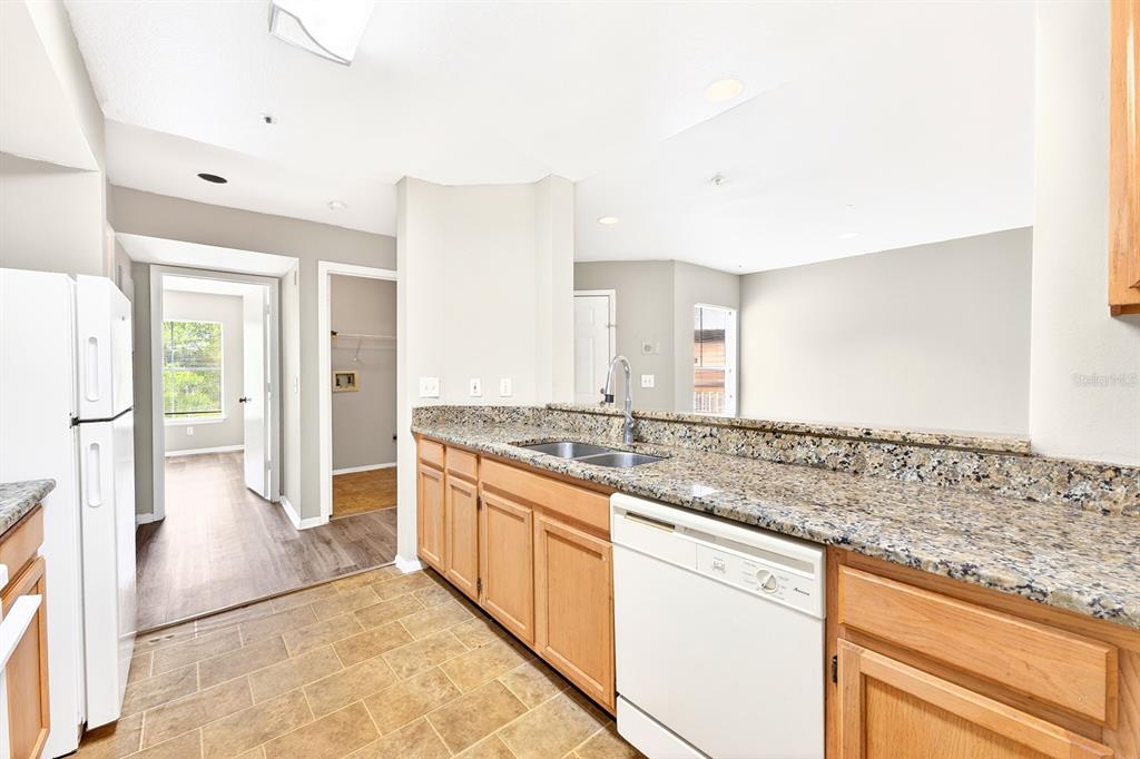 A kitchen features light wood cabinets, granite countertops, a white dishwasher, and tile flooring — 474 S PIN OAK PLACE UNIT 308, LONGWOOD, FL