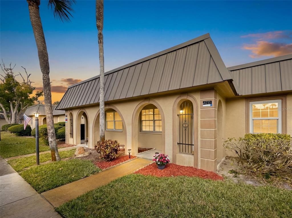 A single-story tan stucco building features arched entryways, a metal roof, and a front walkway — 4233 STRATFORD DRIVE UNIT D, NEW PORT RICHEY, FL