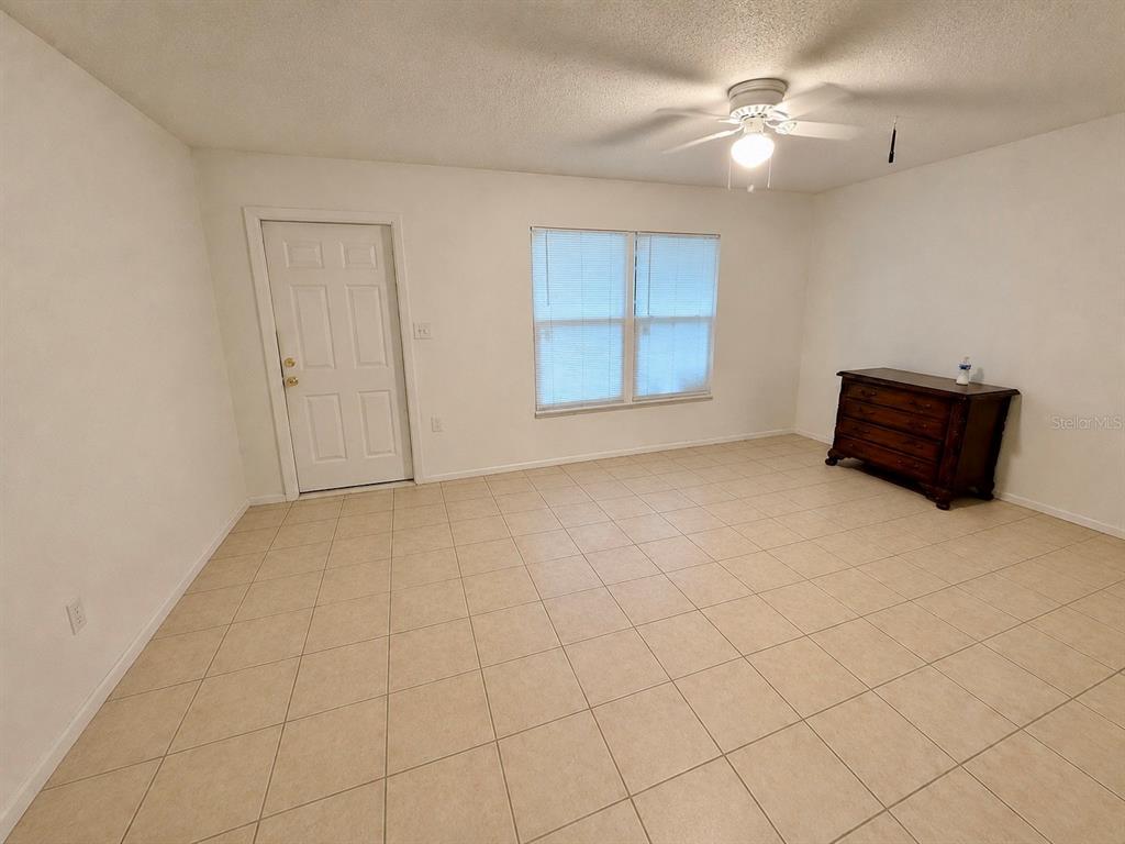 A room with beige tile flooring, a white door, a window with blinds, and a dresser — 3755 AMHERST WAY UNIT 34, SARASOTA, FL