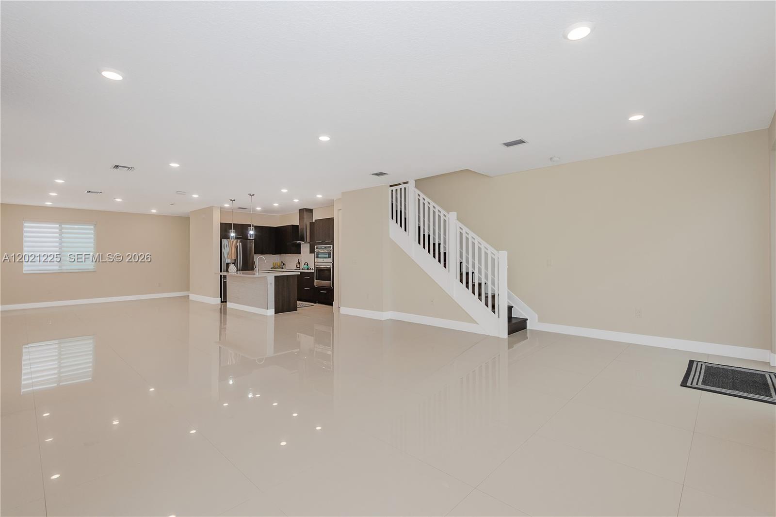 A spacious living area features glossy tile floors, a modern kitchen, and a white staircase — 6681 NW 104th Ave, Doral FL 33178, DORAL, FL
