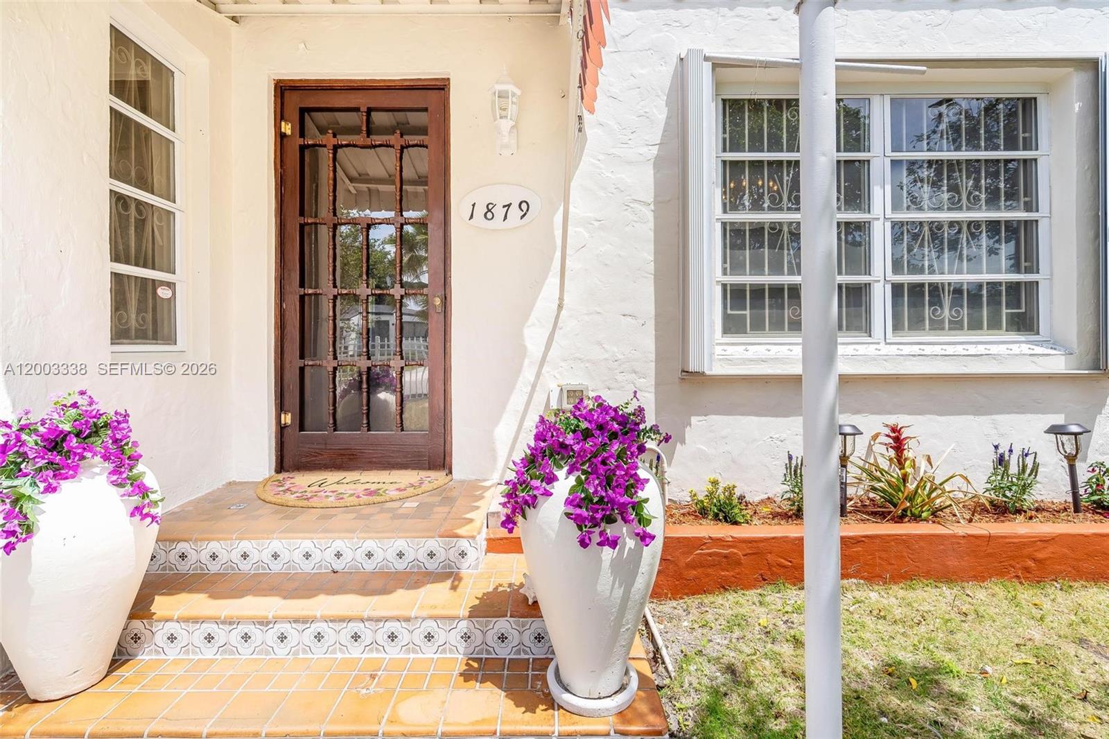 The front entrance features a wooden door, tiled steps, and two large planters with flowers — 1879 SW 16th St, Miami FL 33145, MIAMI, FL