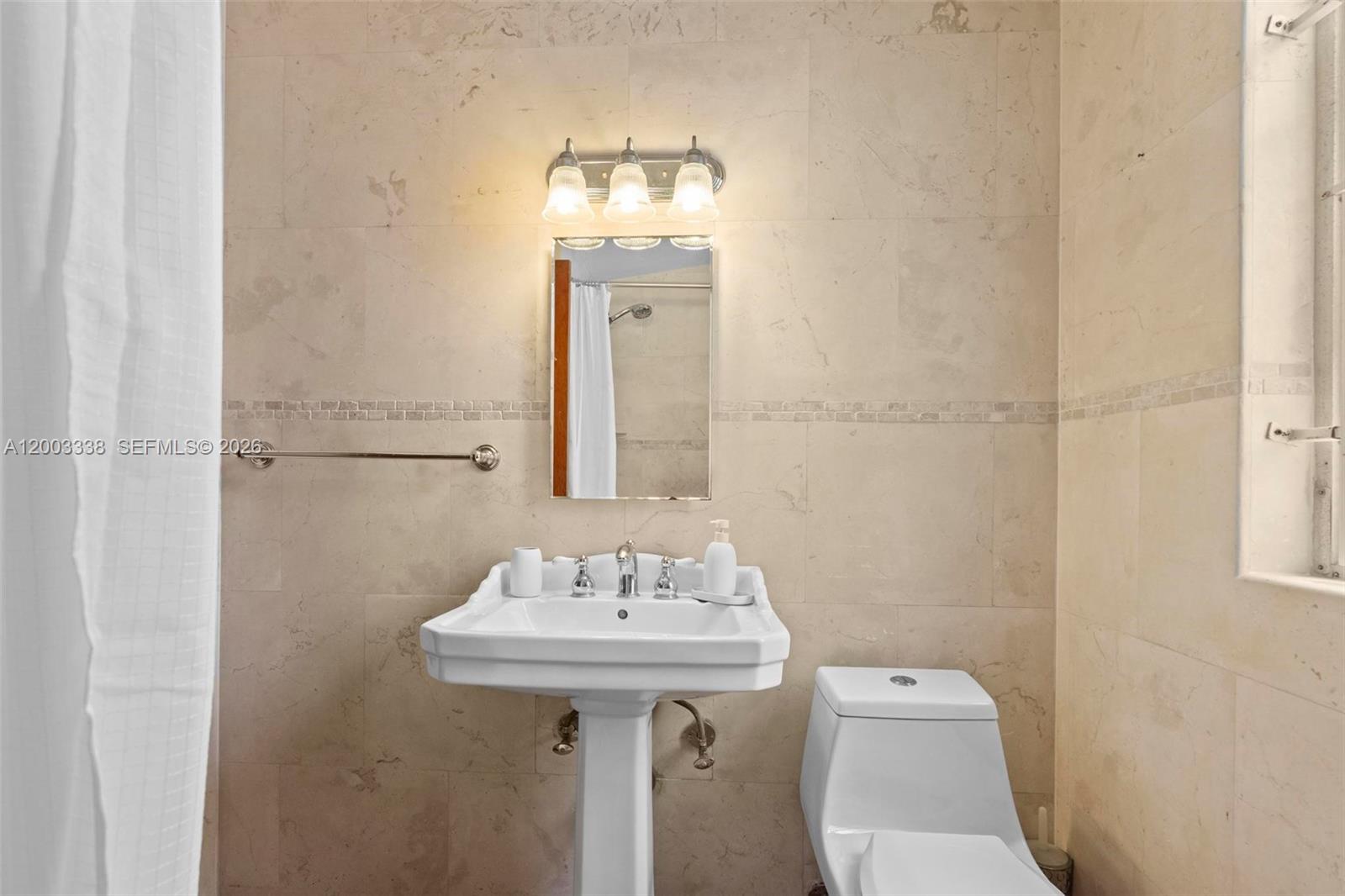 A bathroom features a pedestal sink, a toilet, and a mirror against tiled walls — 1879 SW 16th St, Miami FL 33145, MIAMI, FL