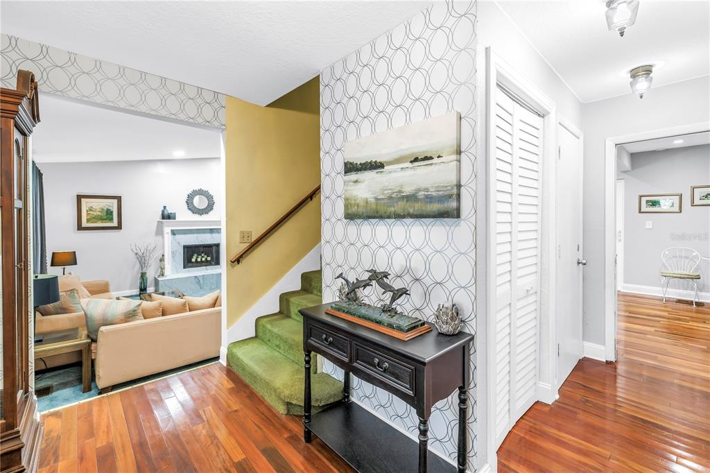 A foyer features green carpeted stairs, patterned wallpaper, a dark console table, and hardwood floors — 6505 CEDAR STREET NE, ST PETERSBURG, FL