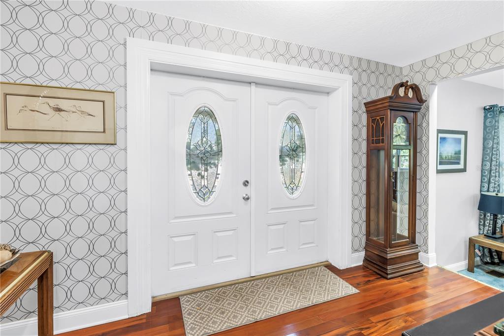 A foyer features double white doors, patterned wallpaper, a grandfather clock, and hardwood flooring — 6505 CEDAR STREET NE, ST PETERSBURG, FL