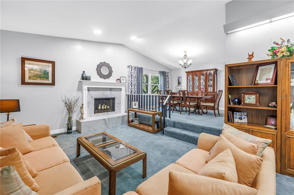 A sunken living room with a fireplace and blue carpeting leads up to a dining area — 6505 CEDAR STREET NE, ST PETERSBURG, FL