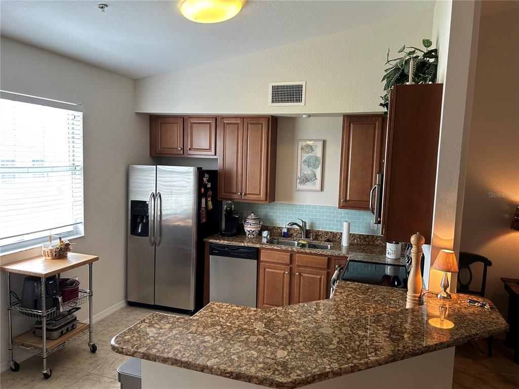 A kitchen features wood cabinets, granite countertops, stainless steel appliances, and a light blue backsplash — 17110 TERRAVERDE CIRCLE UNIT 2415, FORT MYERS, FL