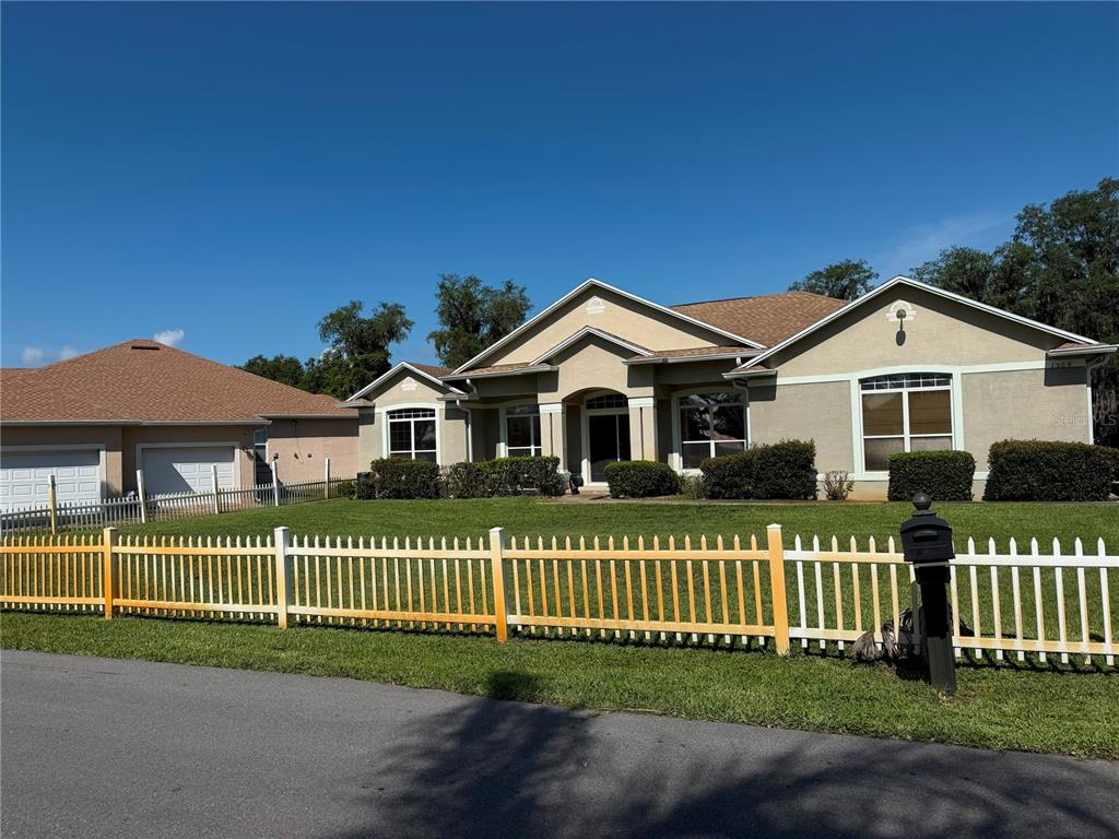 A tan single-story house with a brown roof sits behind a white picket fence — 1504 LAKE THOMAS LOOP, WINTER HAVEN, FL