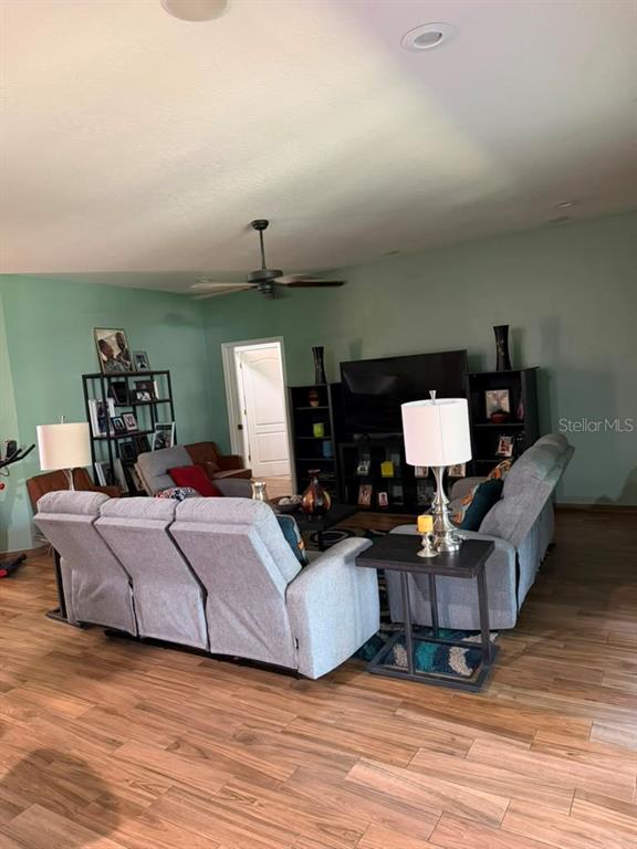 A living room features light gray reclining sofas, wood-look flooring, and a television entertainment center — 1504 LAKE THOMAS LOOP, WINTER HAVEN, FL