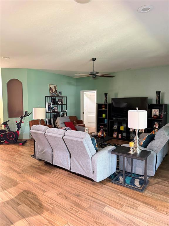 A living room features light green walls, wood-look tile flooring, a sectional sofa, and a television — 1504 LAKE THOMAS LOOP, WINTER HAVEN, FL
