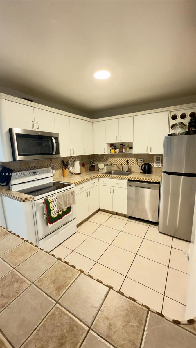 A kitchen with white cabinets, stainless steel appliances, and light-colored tiled floors — 5555 Collins Ave # 16W, Miami Beach FL 33140, MIAMI BEACH, FL