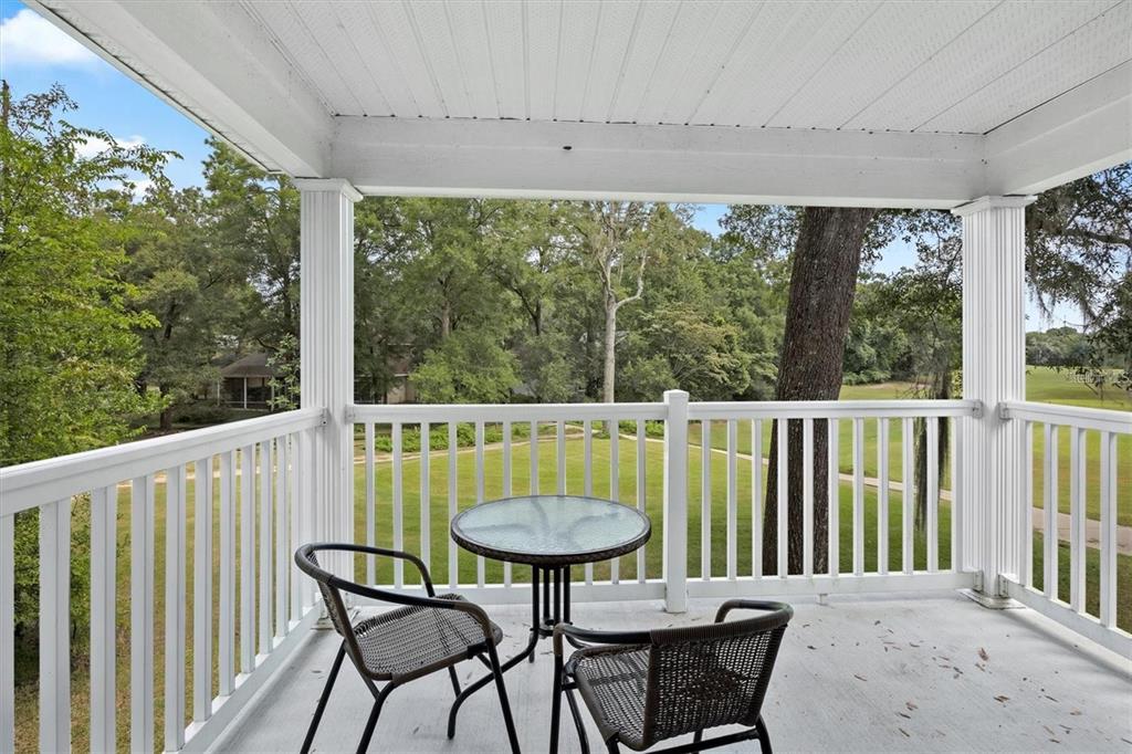 A covered balcony features a glass-topped table and two chairs overlooking a grassy yard — 10000 SW 52ND AVENUE UNIT EE 183, GAINESVILLE, FL