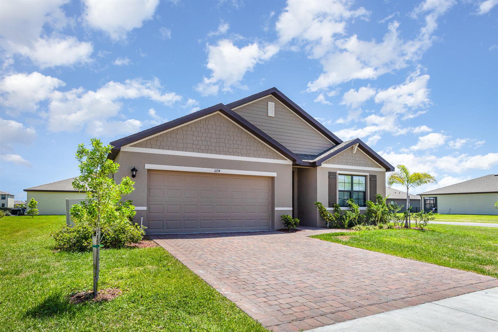 A single-story suburban house features a tan stucco exterior, a brick paver driveway, and shingles — GRANT VALKARIA, FL