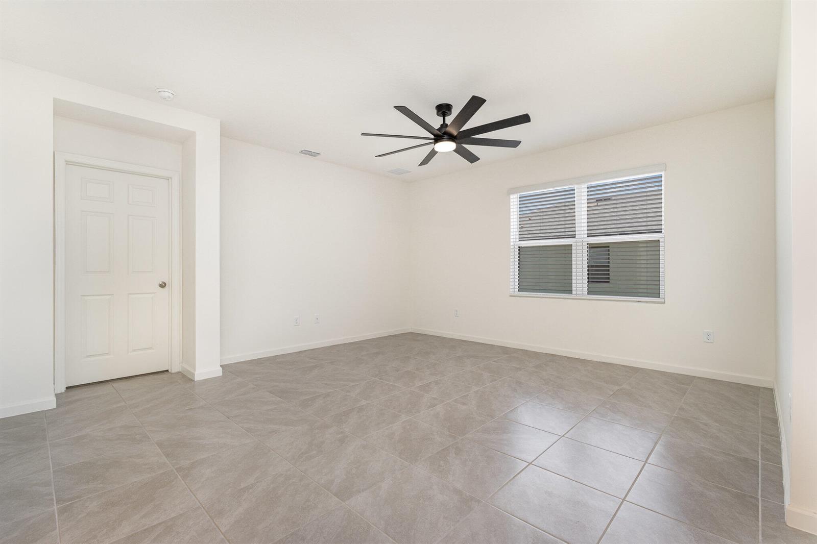 An empty room with white walls, gray tile flooring, a ceiling fan, and a window — GRANT VALKARIA, FL