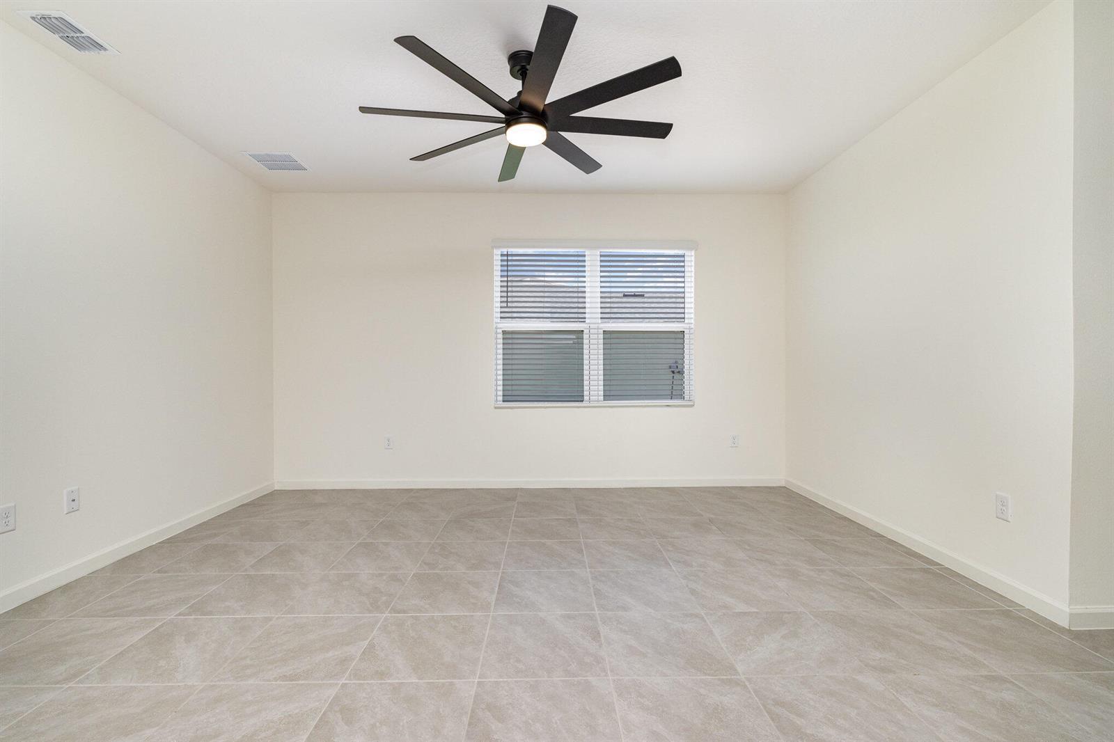 An empty room features light-colored walls, large gray floor tiles, and a black ceiling fan — GRANT VALKARIA, FL