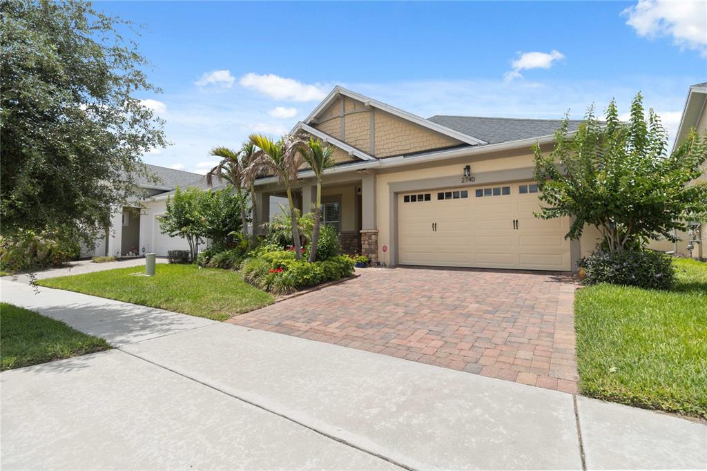 A single-story house with a beige garage, stone accents, and a brick paver driveway — 2740 SOUTHLAND STREET, ST CLOUD, FL