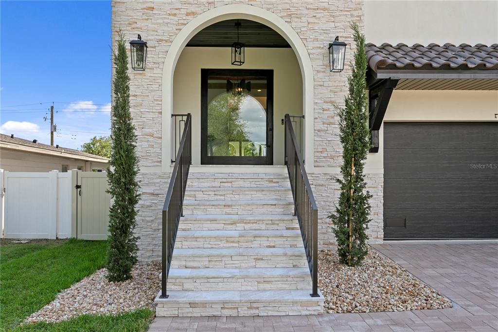 A stone-faced house exterior features an arched entryway with stairs and two tall, thin trees — 502 E DAVIS BOULEVARD, TAMPA, FL