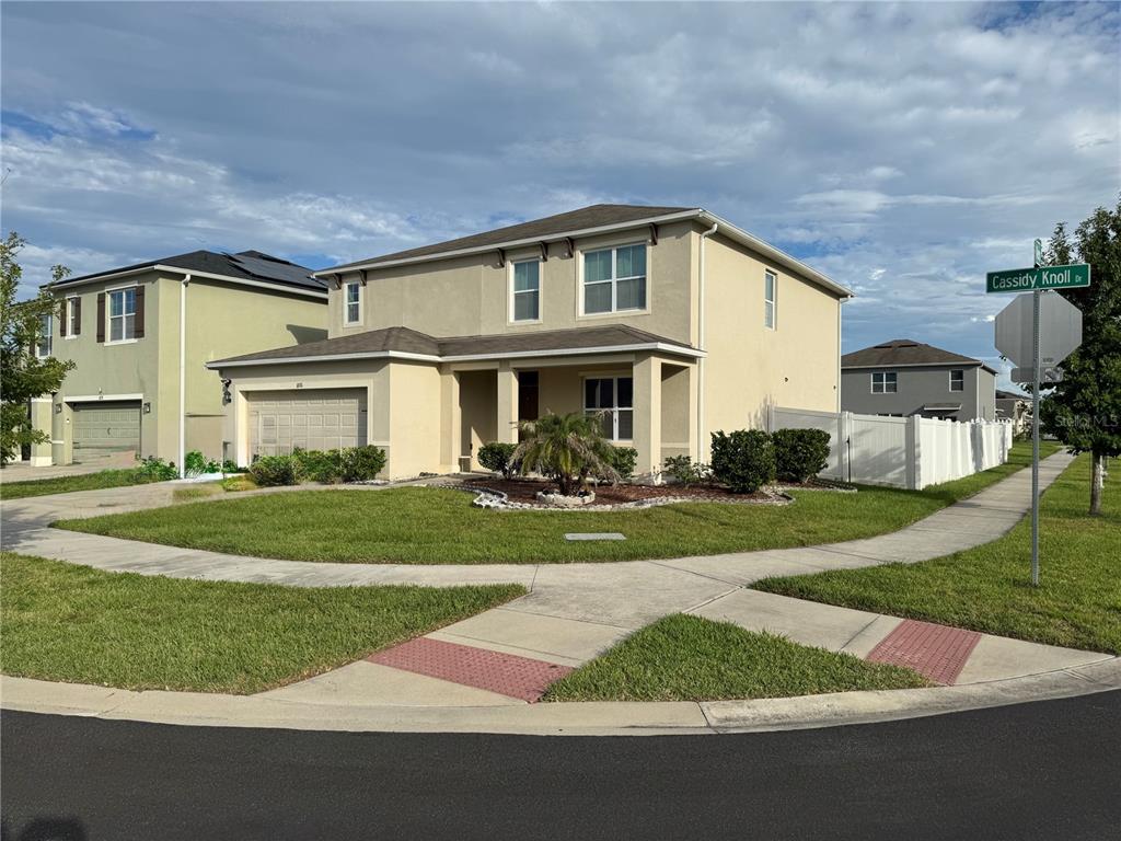 A two-story tan house with a two-car garage sits on a corner lot — 1876 CASSIDY KNOLL DRIVE, KISSIMMEE, FL