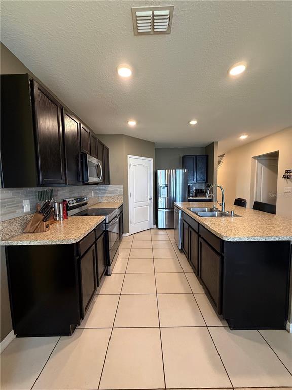 A kitchen features dark wood cabinets, granite countertops, stainless steel appliances, and light tile flooring — 1876 CASSIDY KNOLL DRIVE, KISSIMMEE, FL
