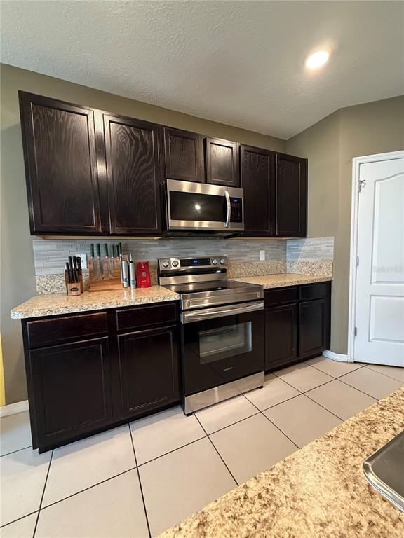 A kitchen features dark wood cabinets, stainless steel appliances, and speckled granite countertops — 1876 CASSIDY KNOLL DRIVE, KISSIMMEE, FL