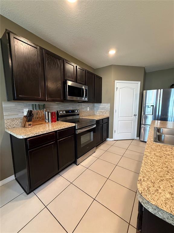 A kitchen features dark wood cabinets, granite countertops, stainless steel appliances, and light tile flooring — 1876 CASSIDY KNOLL DRIVE, KISSIMMEE, FL