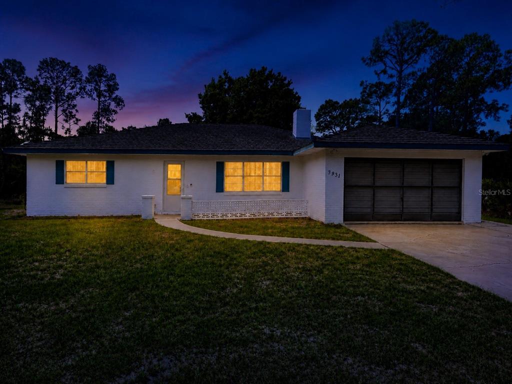 A single-story white brick house with a blue roof and a garage sits on grass — 3931 GAILLARDIA DRIVE, INDIAN LAKE ESTATES, FL