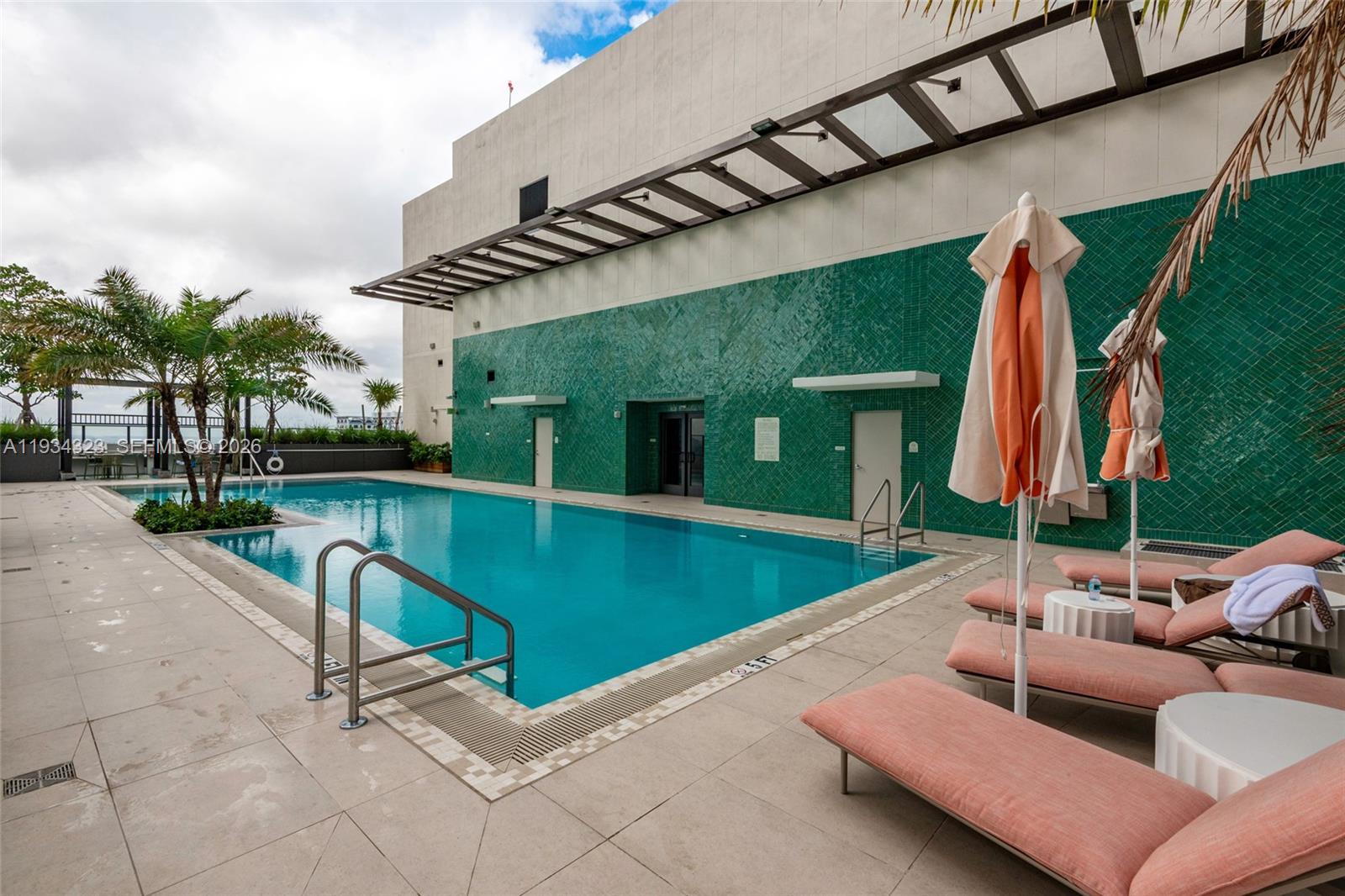 A swimming pool with a green tiled wall and lounge chairs on a paved deck — 11 NE 6 ST # 1407, Miami FL 33132, MIAMI, FL