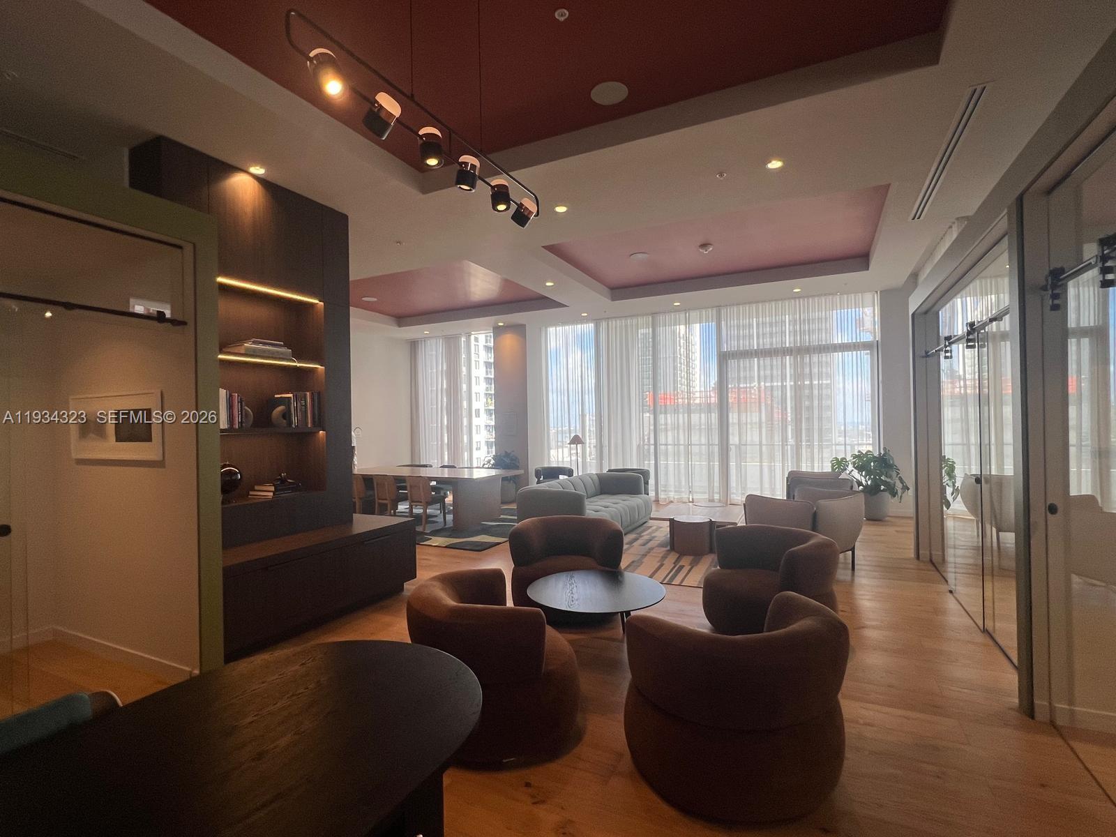 A modern lounge area features brown armchairs, a central coffee table, and floor-to-ceiling windows — 11 NE 6 ST # 1407, Miami FL 33132, MIAMI, FL