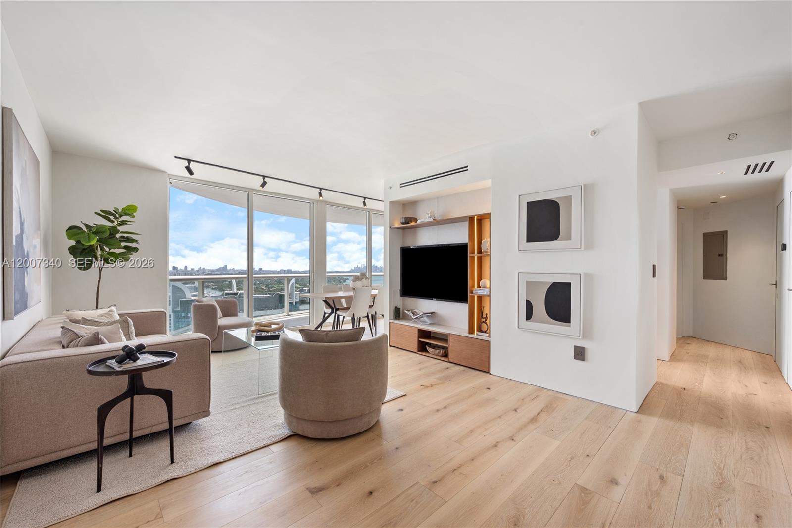 A modern living room features light wood floors, a built-in media unit, and floor-to-ceiling windows — 6365 Collins Ave # 3904, Miami Beach FL 33141, MIAMI BEACH, FL