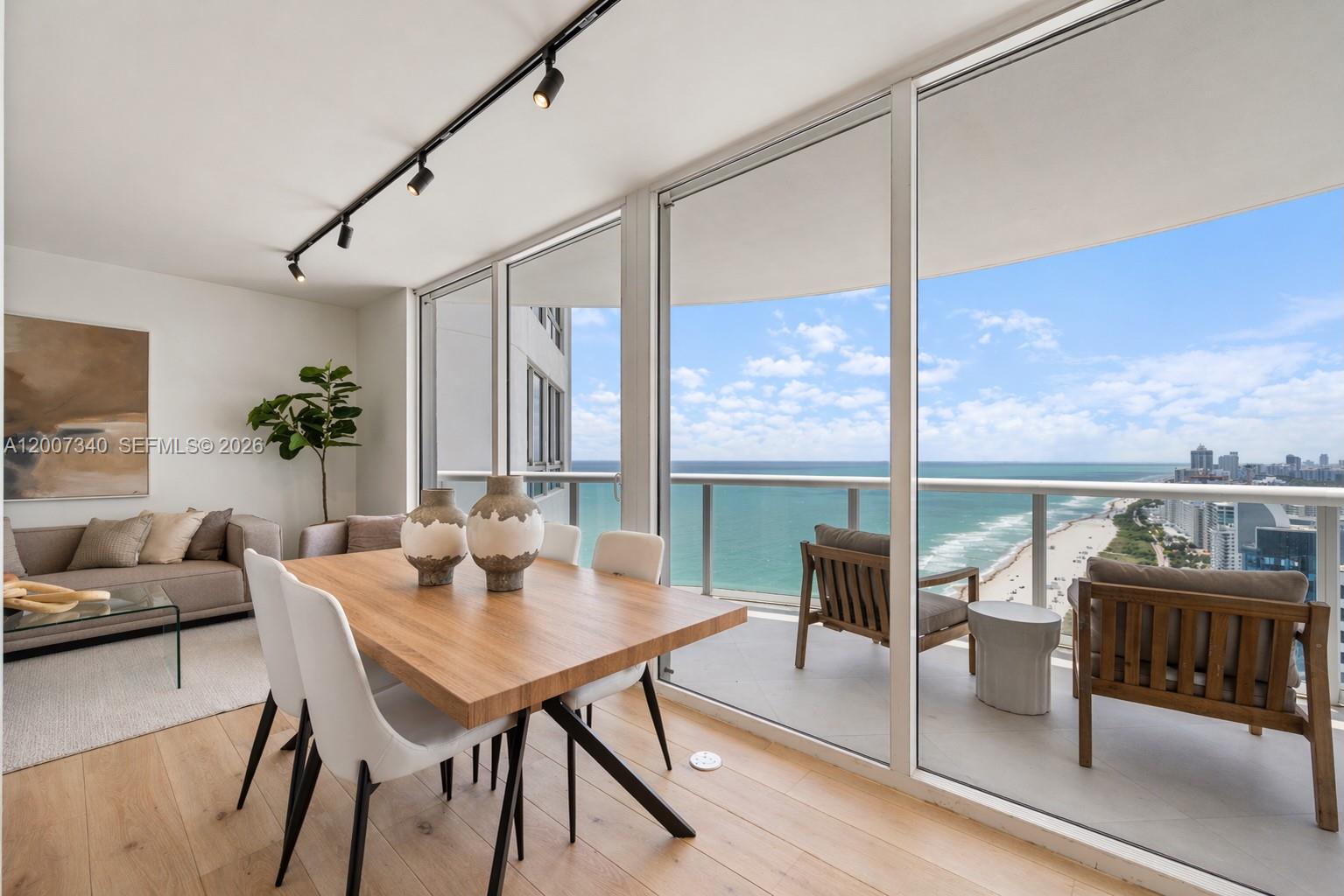 A dining area with a wooden table and chairs overlooks a balcony and the ocean — 6365 Collins Ave # 3904, Miami Beach FL 33141, MIAMI BEACH, FL