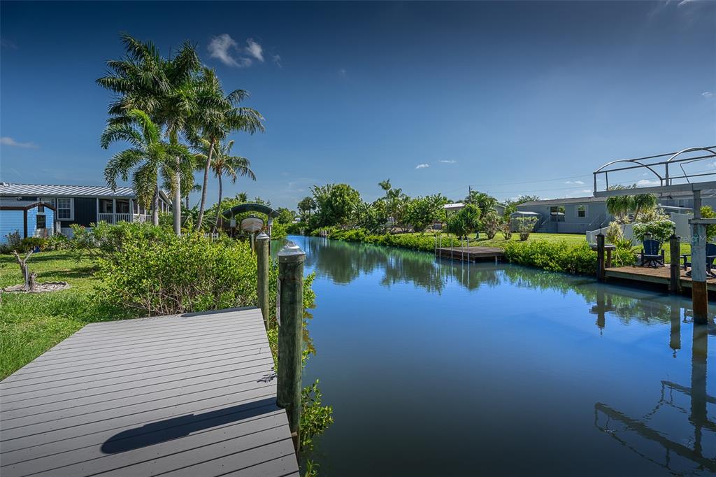 A wooden dock extends into a narrow canal lined with palm trees and residential homes — 3118 BAYBERRY AVENUE, PUNTA GORDA, FL