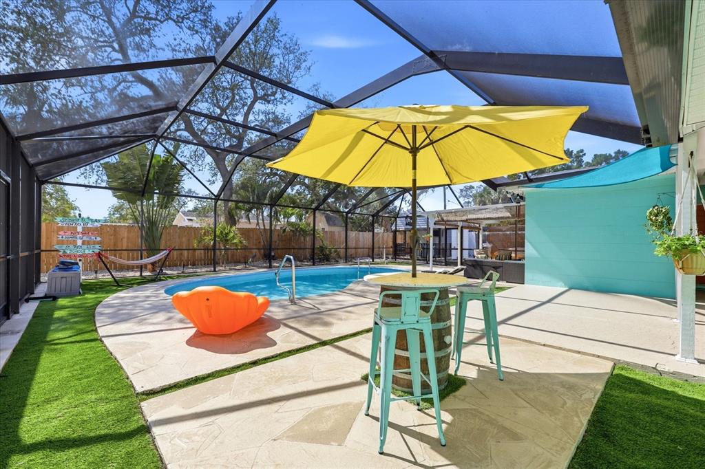 A screened-in patio features a swimming pool, a yellow umbrella, and a barrel table — 712 S GLENWOOD AVENUE, CLEARWATER, FL