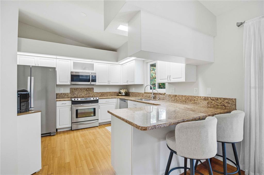 A kitchen features white cabinets, granite countertops, stainless steel appliances, and a breakfast bar — 3131 ARROWHEAD ROAD, VENICE, FL
