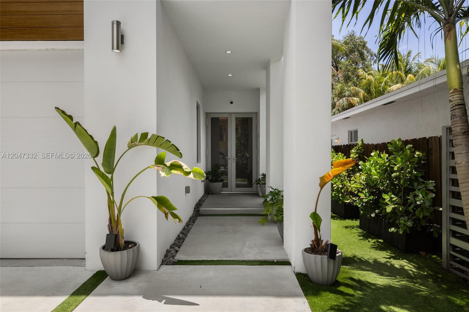 A modern home entrance features a concrete walkway, white walls, and potted tropical plants — 3139 Ohio St # 3139, Coconut Grove FL 33133, COCONUT GROVE, FL