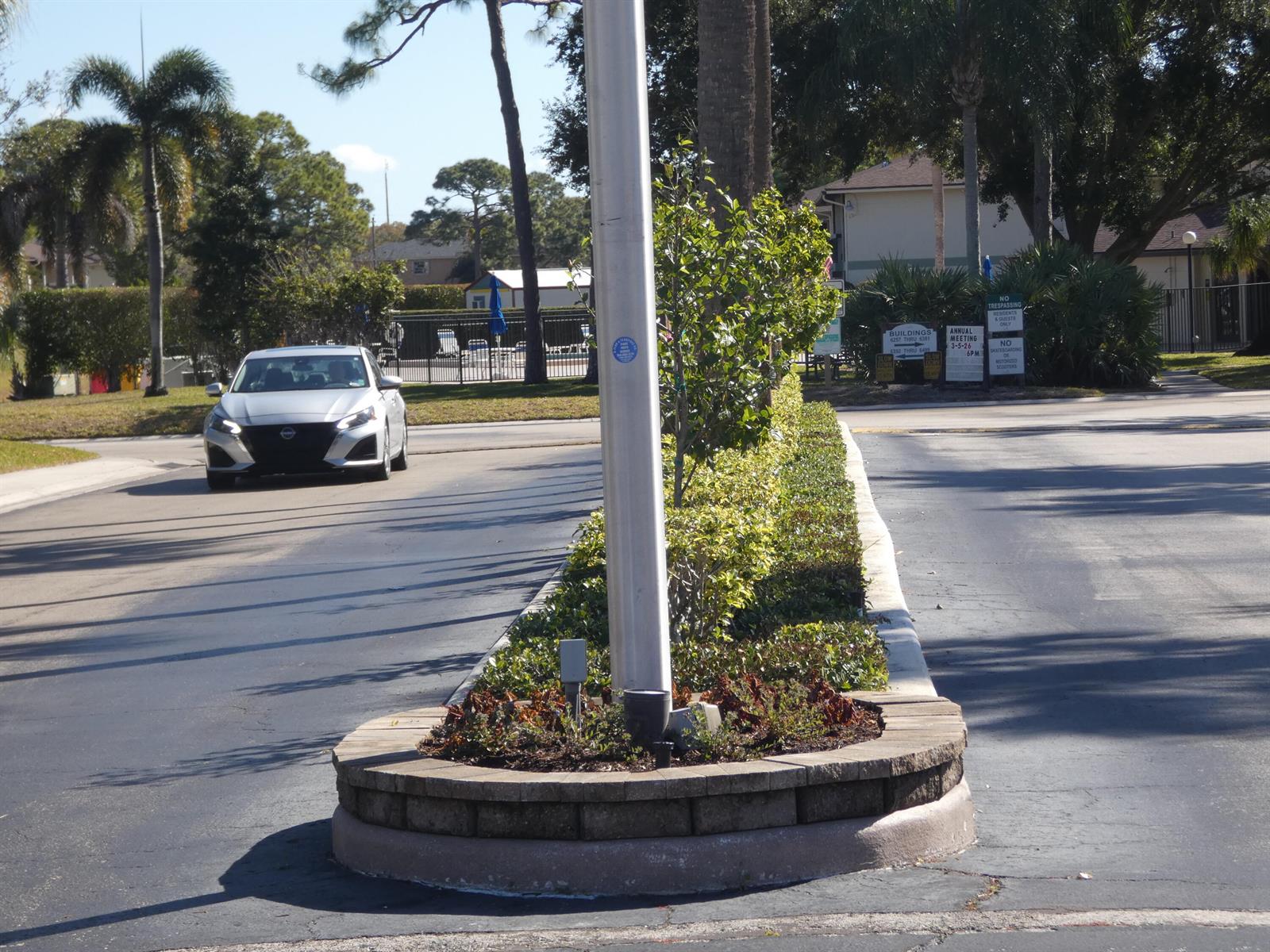 A silver car approaches a landscaped median with a light pole in a residential area — 6495 SE Chasewood Drive, Jupiter FL 33458, JUPITER, FL