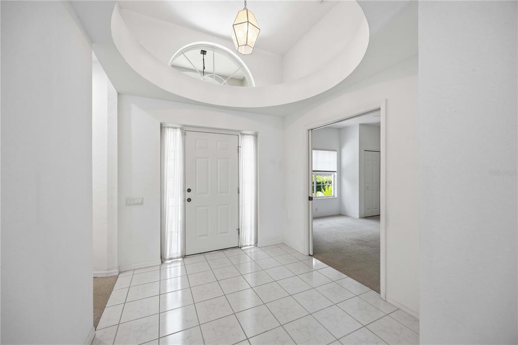 A bright entryway features white tiled floors, a high arched ceiling, and a glass-paneled door — 7159 PRESTWICK COURT, UNIVERSITY PARK, FL