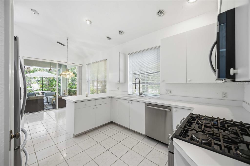 A white kitchen features stainless steel appliances, tile flooring, and a view of a patio — 7159 PRESTWICK COURT, UNIVERSITY PARK, FL