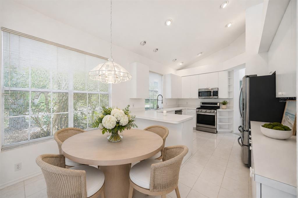 A bright kitchen and dining area with white cabinetry, stainless steel appliances, and tile flooring — 7159 PRESTWICK COURT, UNIVERSITY PARK, FL