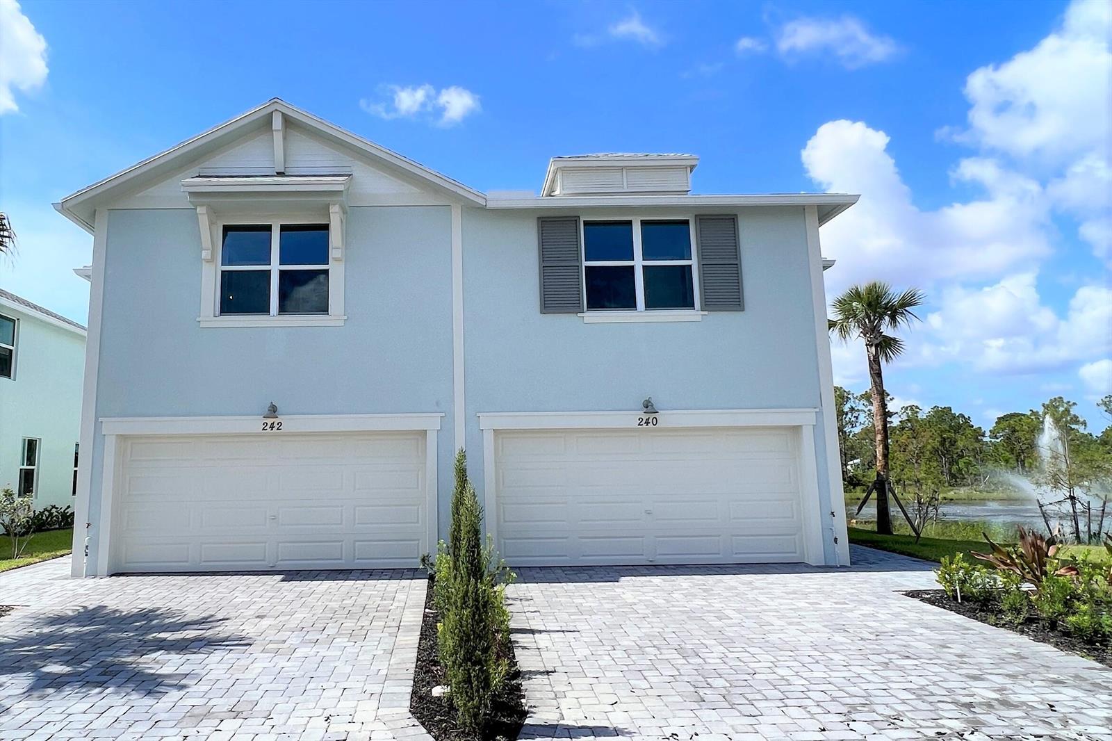 A two-story duplex with light blue siding, two white garage doors, and a paved driveway — 240 Osprey Preserve Boulevard, Jensen Beach FL 34957, JENSEN BEACH, FL