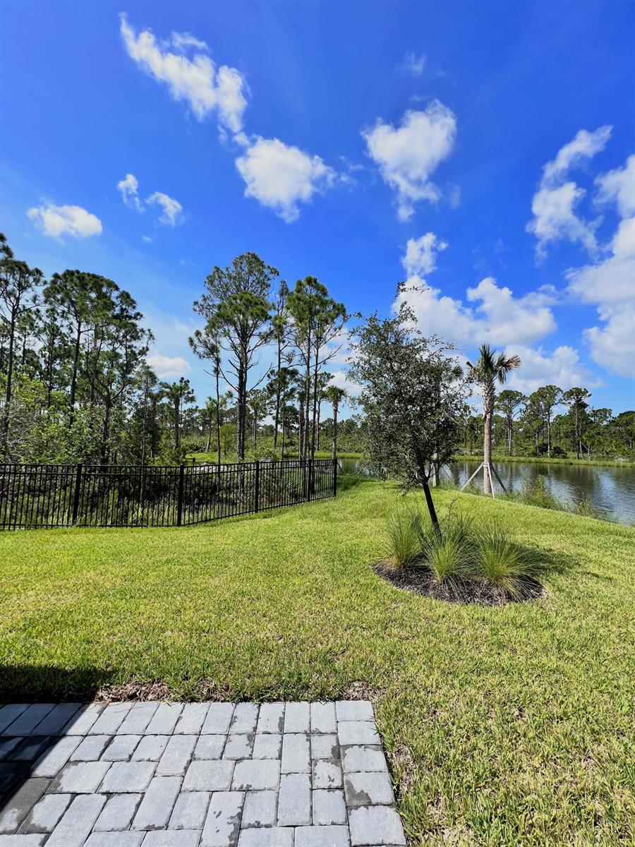 A paved patio overlooks a grassy lawn, a black metal fence, and a pond — 240 Osprey Preserve Boulevard, Jensen Beach FL 34957, JENSEN BEACH, FL