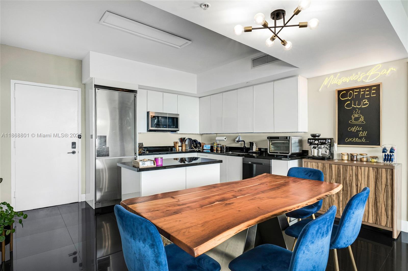 A modern kitchen features white cabinetry, black countertops, a wooden dining table, and blue chairs — 92 SW 3rd St # 4312, Miami FL 33130, MIAMI, FL
