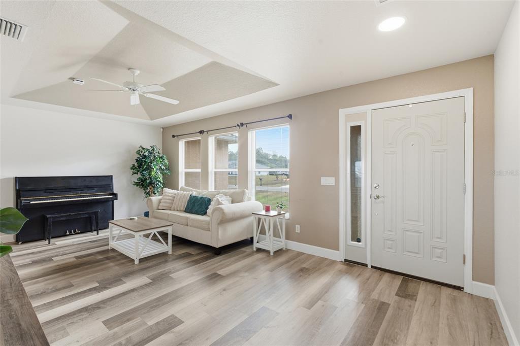 A living room features a piano, a white sofa, wood-look flooring, and a front door — 4409 KENOSKA STREET, NORTH PORT, FL