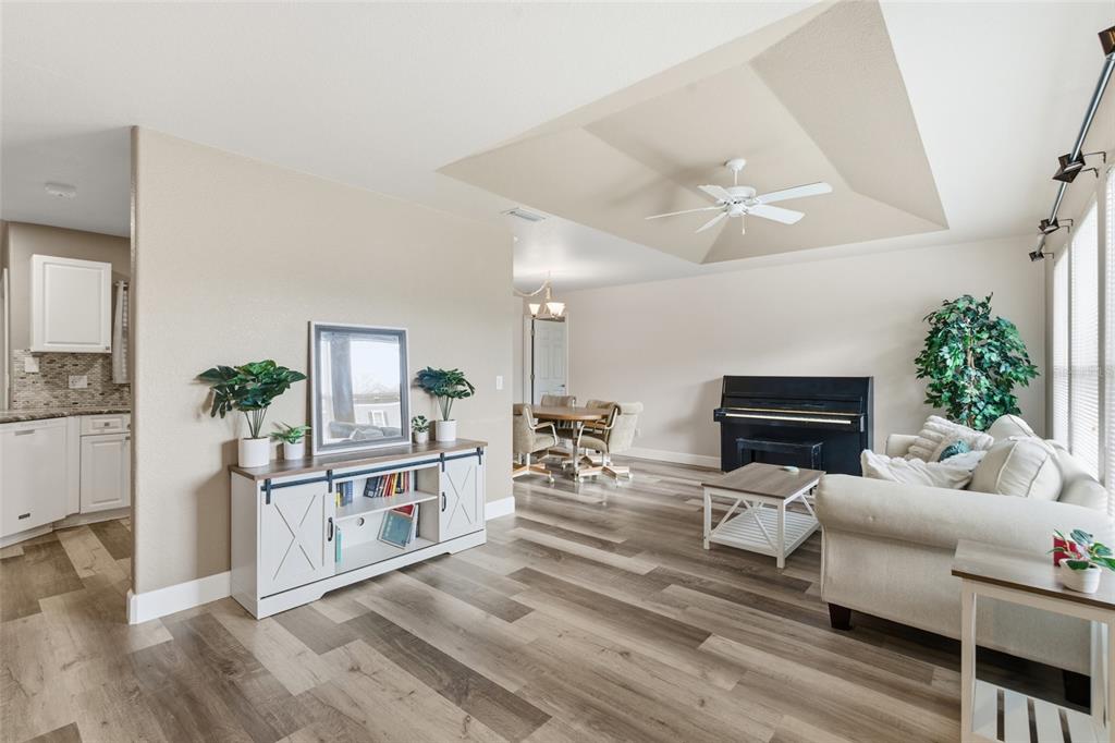A living room features wood-look flooring, a tray ceiling with a fan, and a piano — 4409 KENOSKA STREET, NORTH PORT, FL