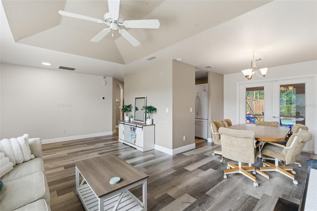 A living and dining area with vaulted ceilings, wood-look flooring, and a white ceiling fan — 4409 KENOSKA STREET, NORTH PORT, FL