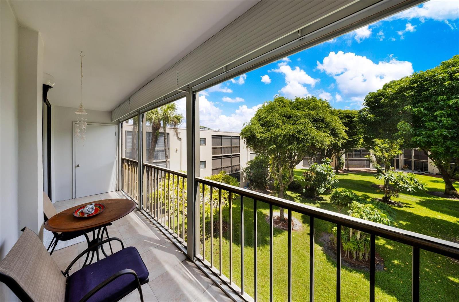 A balcony with a small table and chairs overlooks a grassy courtyard with trees — 5250 Las Verdes Circle # 317, Delray Beach FL 33484, DELRAY BEACH, FL