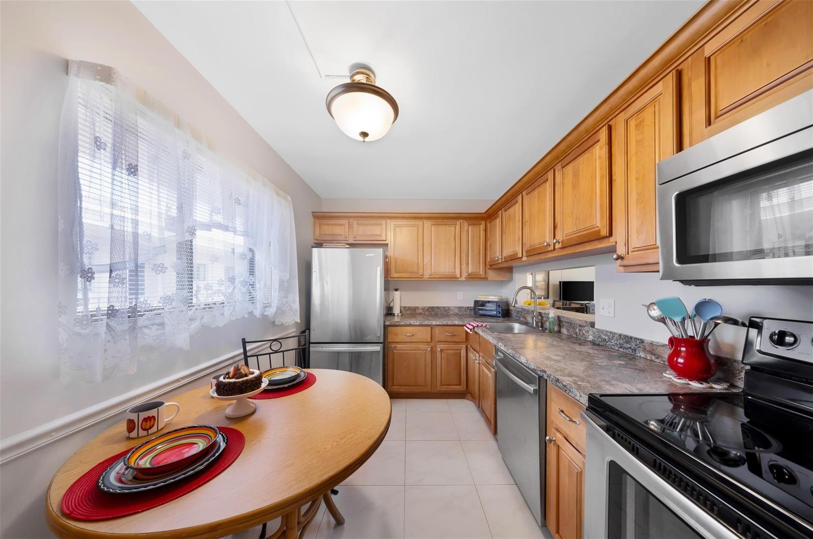 A kitchen with wood cabinets, stainless steel appliances, and a round wooden dining table — 5250 Las Verdes Circle # 317, Delray Beach FL 33484, DELRAY BEACH, FL