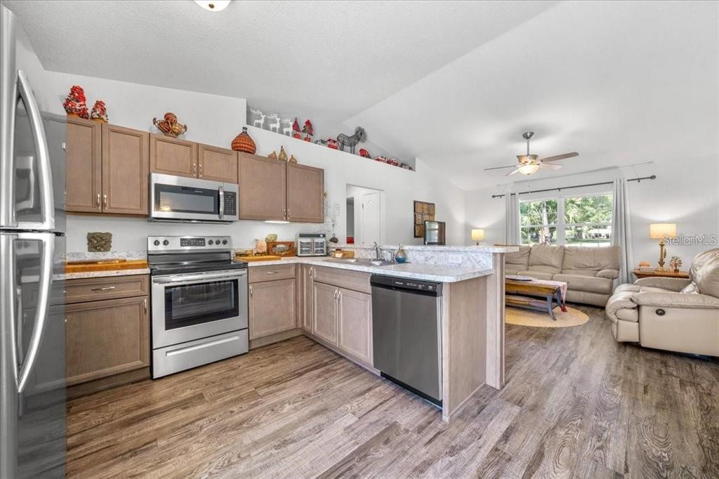 A kitchen with wood cabinets and stainless steel appliances opens into a living room area — 543 N ROOKS AVENUE, INVERNESS, FL