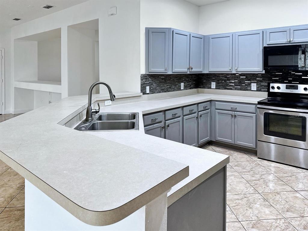 A kitchen features grey cabinets, stainless steel appliances, a tiled backsplash, and a light-colored countertop — 2024 BEARING LANE, KISSIMMEE, FL