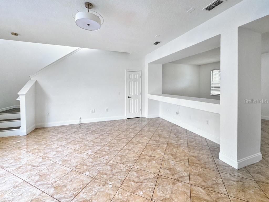 An empty room features beige tile flooring, white walls, a staircase, and a pass-through window — 2024 BEARING LANE, KISSIMMEE, FL